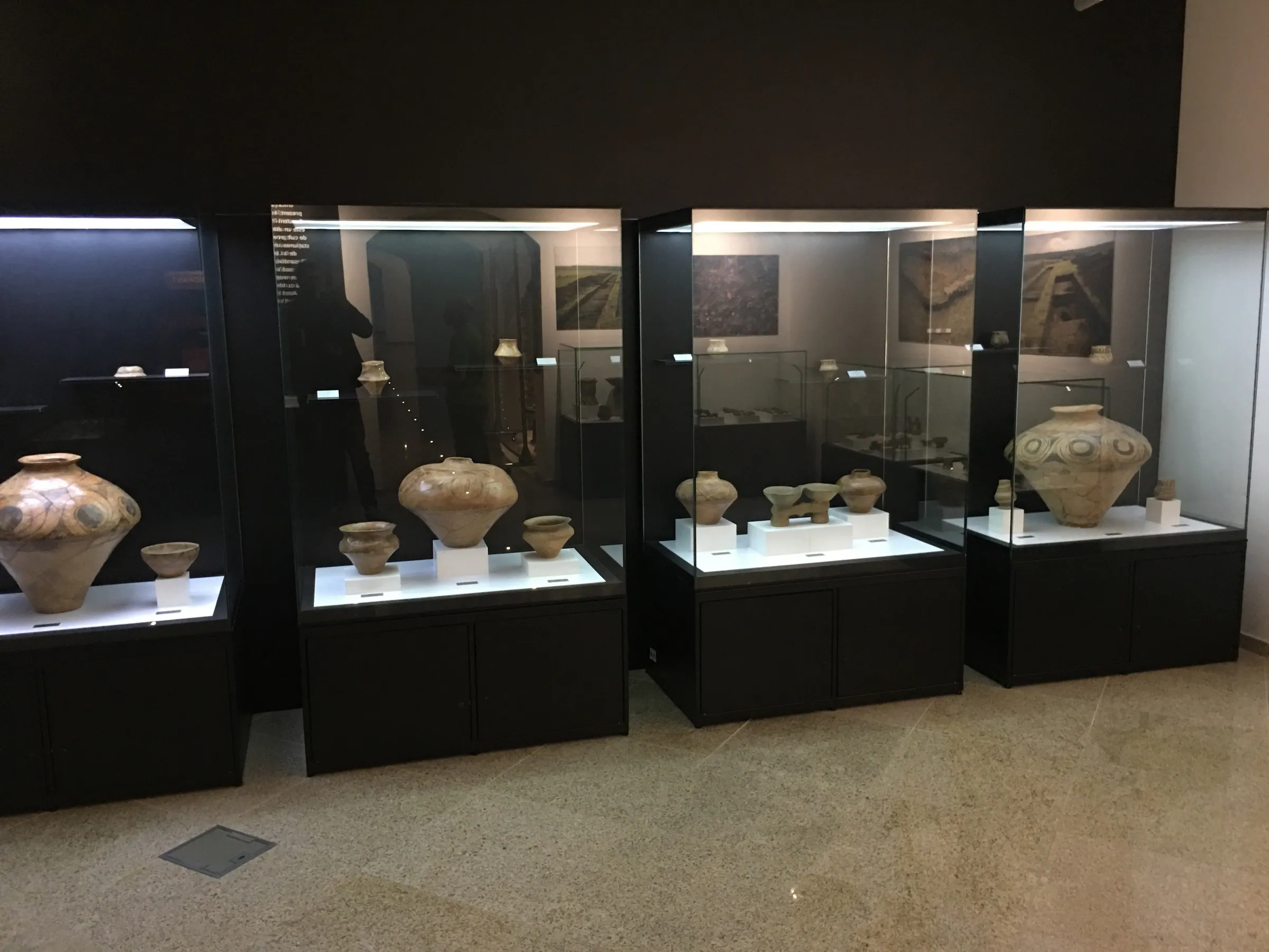 Șir de vitrine iluminate cu vase de ceramică pictată, pe socluri negre